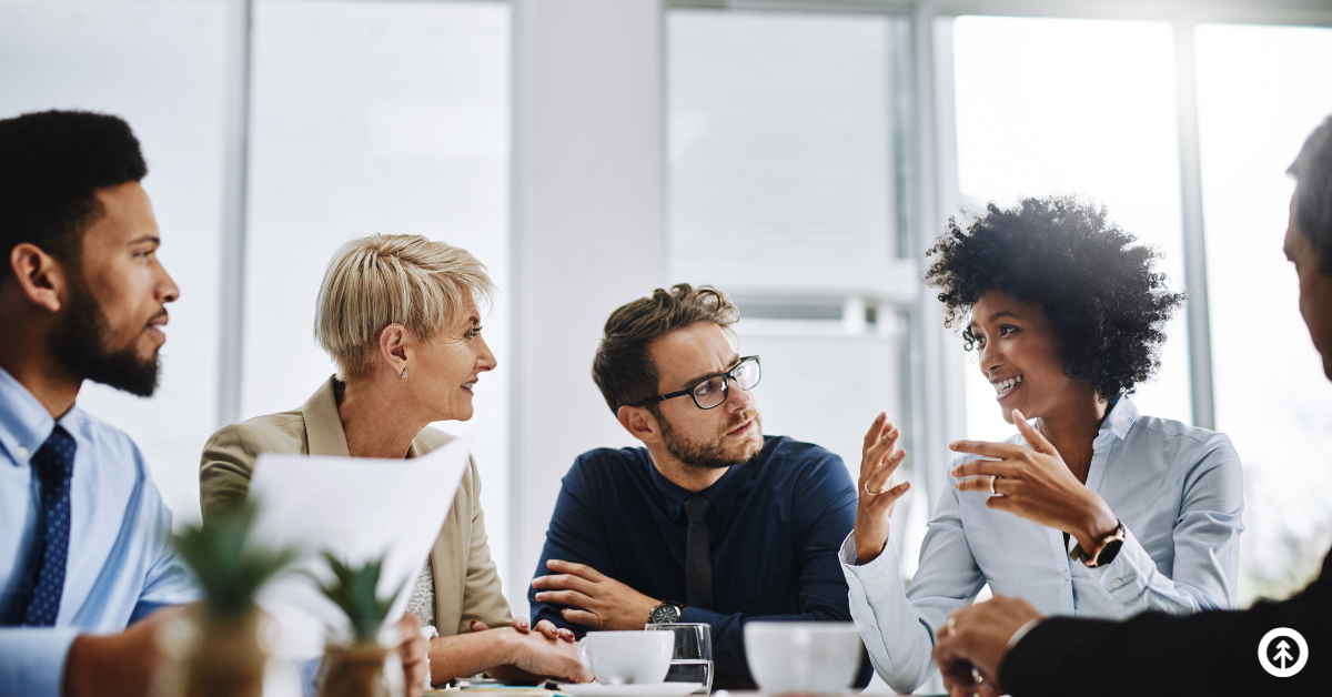 A group of people sitting around a conference table listening intently to one person speaking.