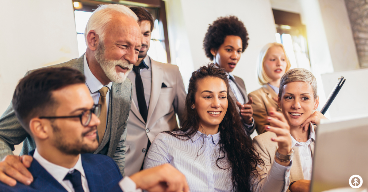A group of co-workers looking at good news on a computer screen and smiling.