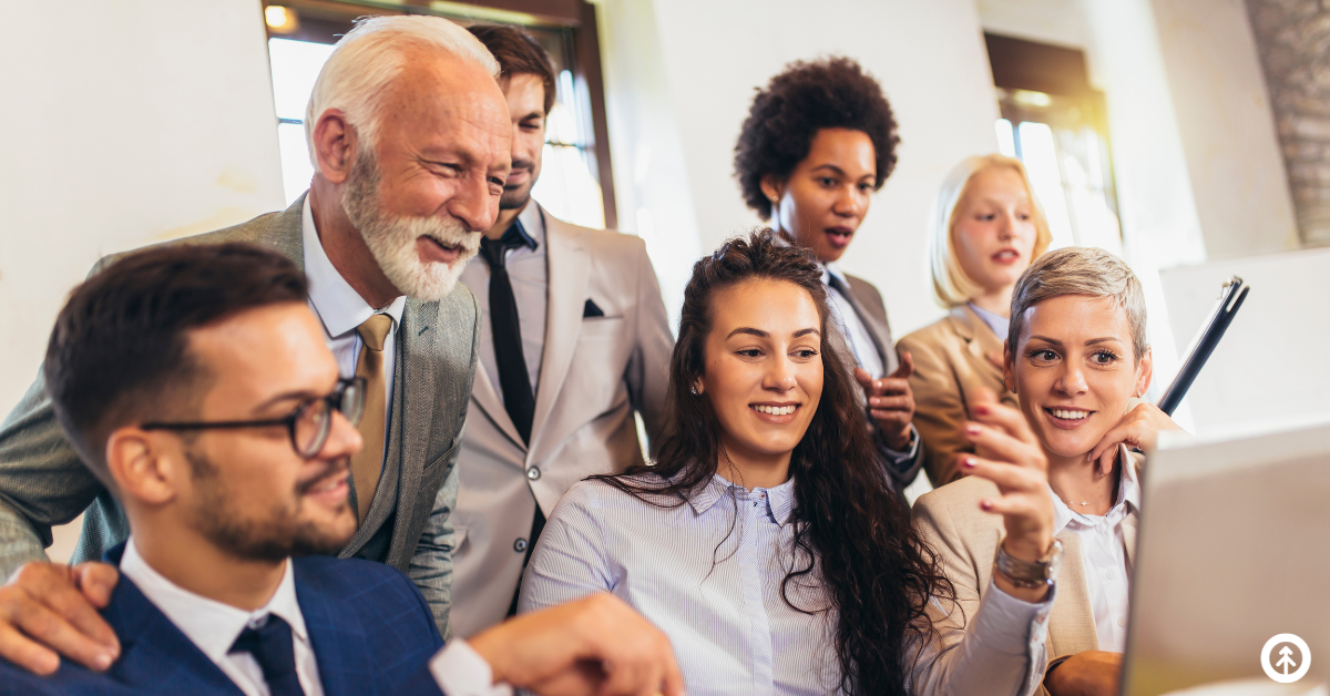 A group of co-workers looking at good news on a computer screen and smiling. 