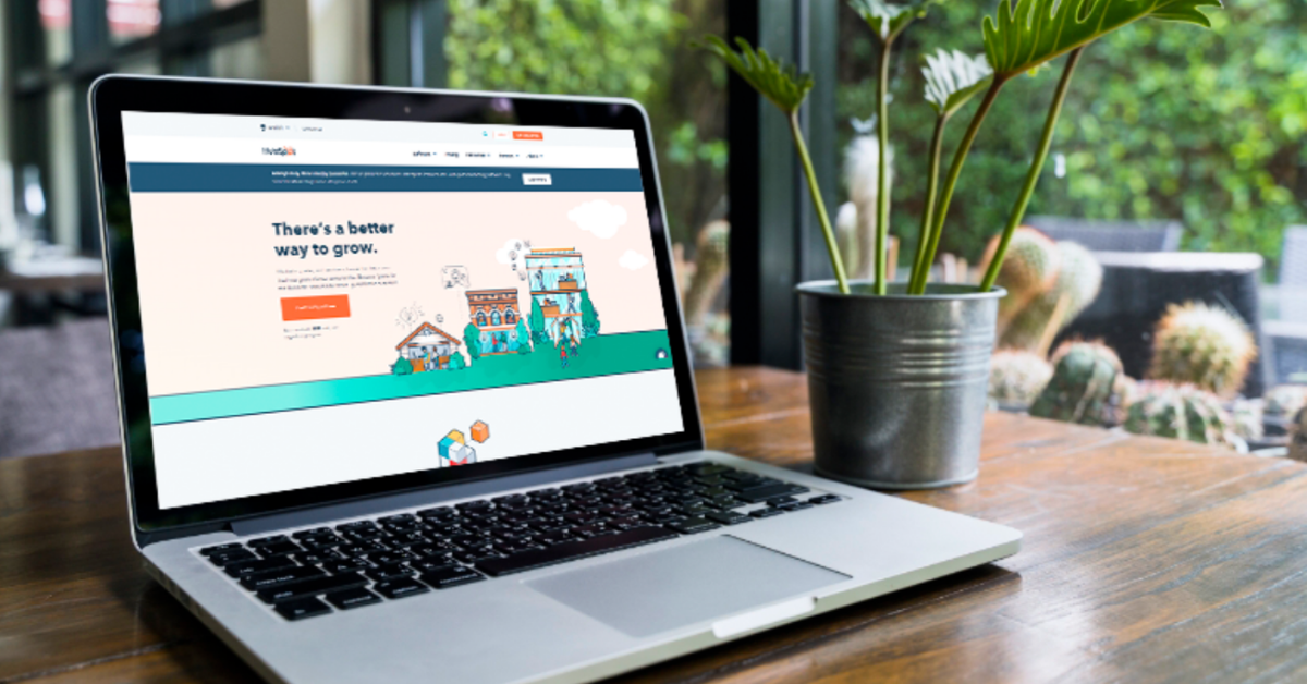 A laptop open on a wooden workspace table with the HubSpot website showing on the screen.