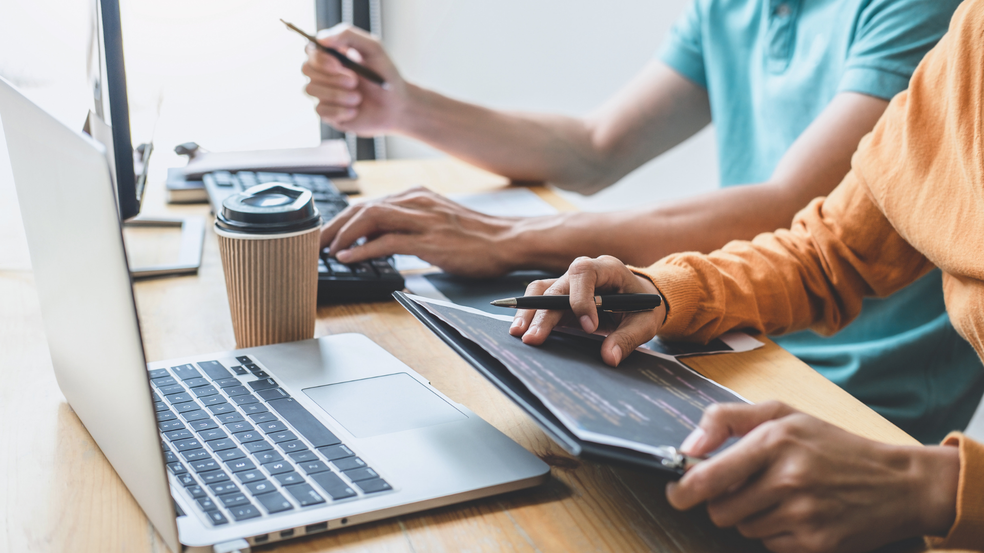 Two people working together side-by-side to analyze data on laptop computers. 