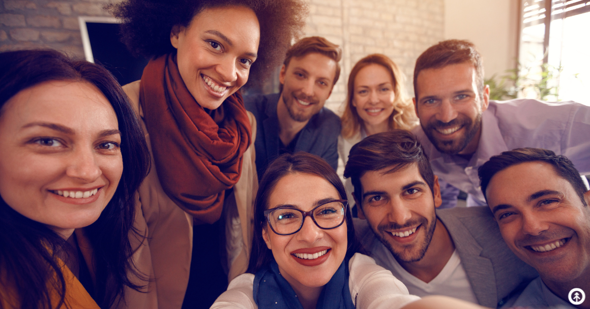 A group of people in an office setting smiling while taking a selfie together.