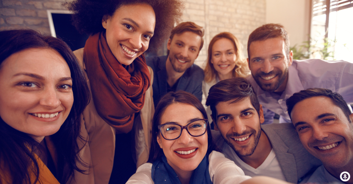 A group of people in an office setting smiling while taking a selfie together. 