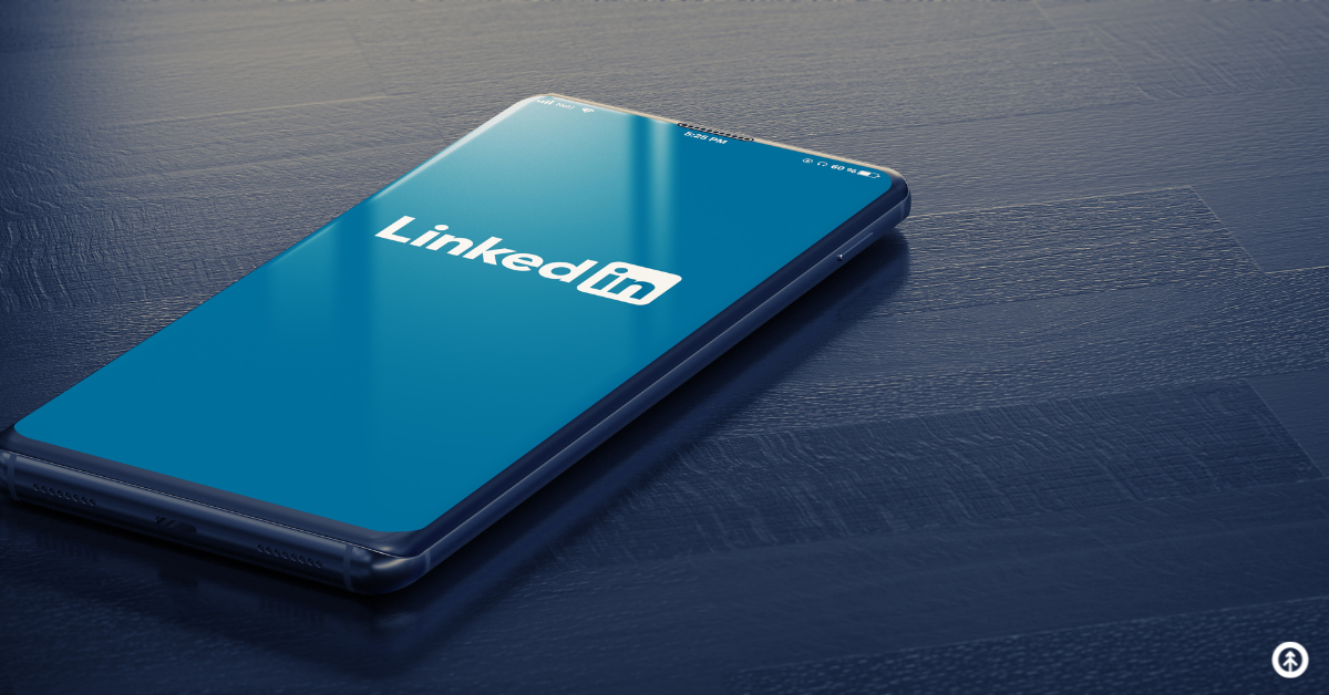 A mobile phone lying flat on a blue wooden table with LinkedIn open on the screen.