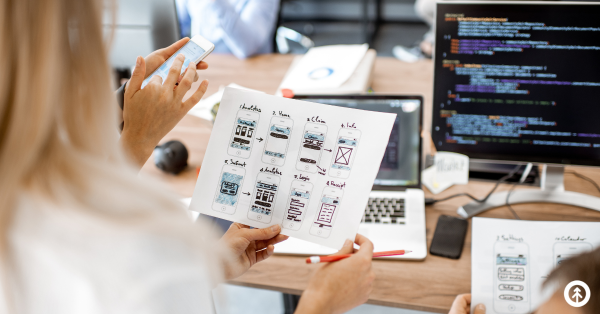 Website designers holding paper examples of UX design concepts for a website's mobile user experience.