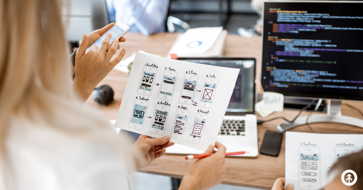 Website designers holding paper examples of UX design concepts for a website's mobile user experience. 