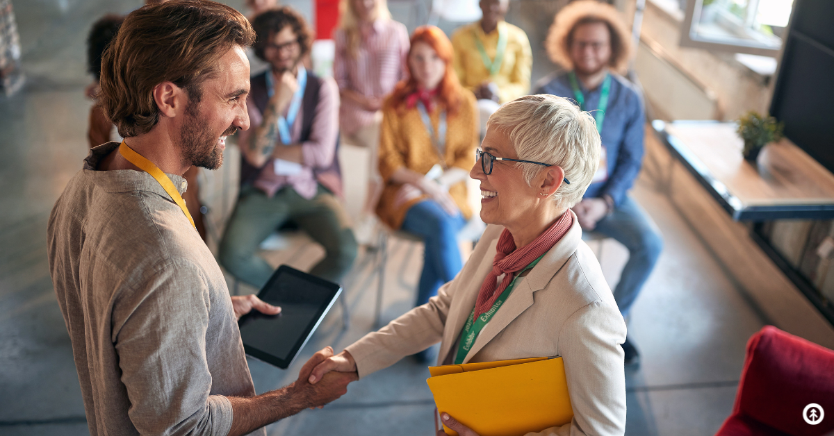 Two people shaking hands in front of an audience. 