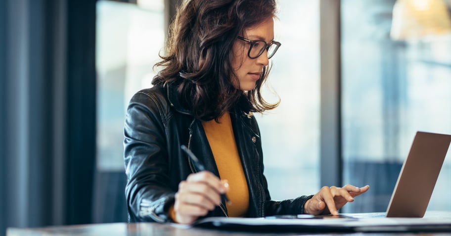 A business woman conducting an internet search on a laptop computer while taking notes