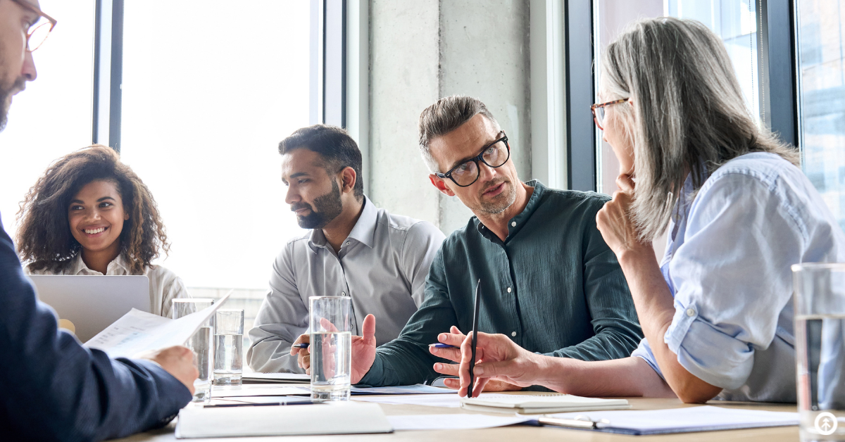 Five professionals sharing ideas in a board room with large windows all around them. 