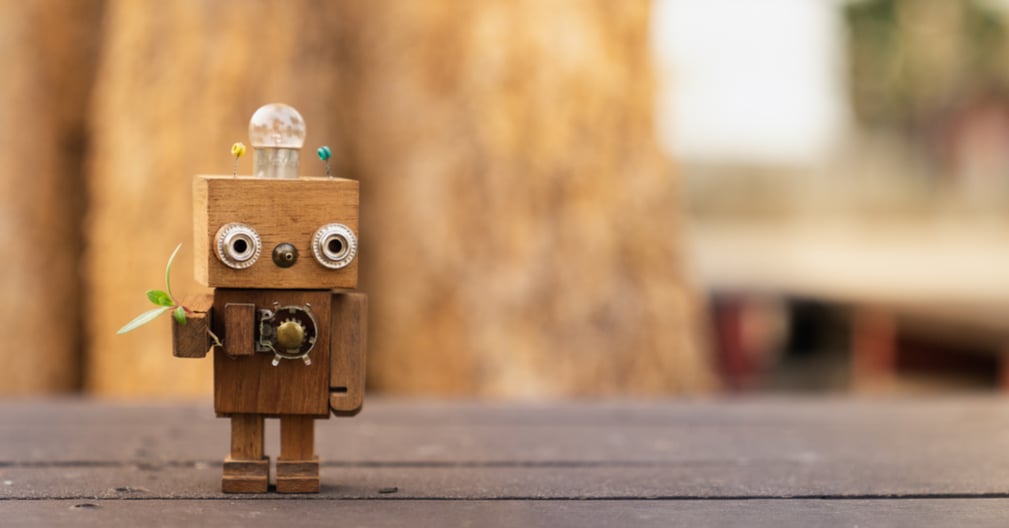An adorable wooden toy robot with a plant in one hand.