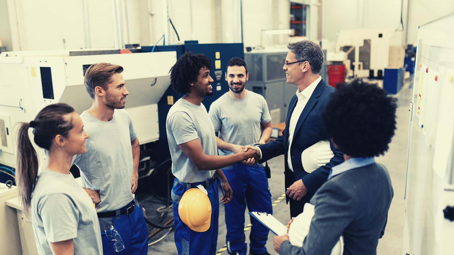 A happy customer shakes hands with workers while on a factory tour. 