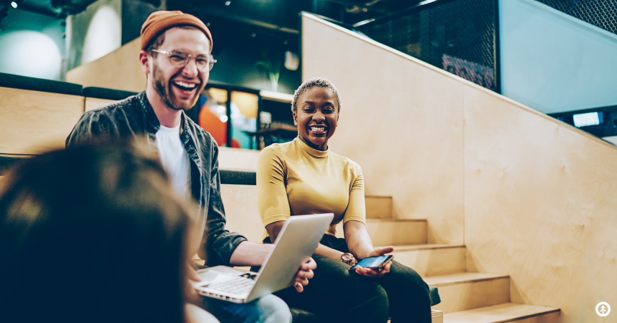 Two really happy friends laughing together while sitting in bleachers with their devices on. 