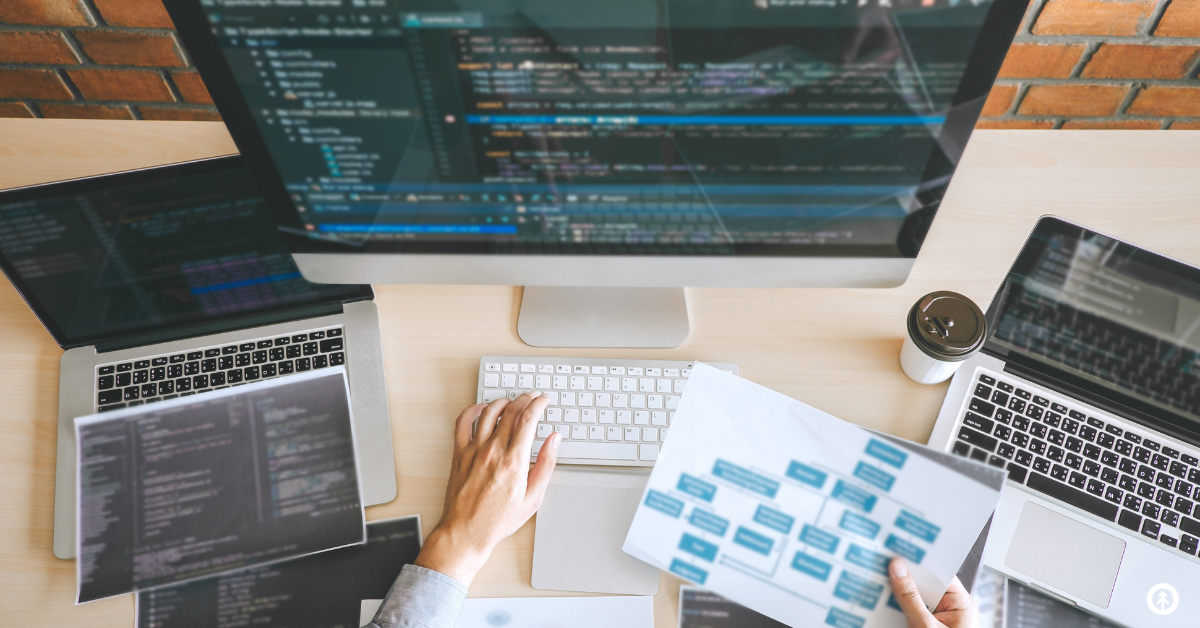 A website developer creating a site on a desktop computer while aligning code with multiple laptops.