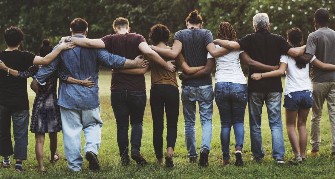 A group of diverse people walking together arm-in-arm toward the sun