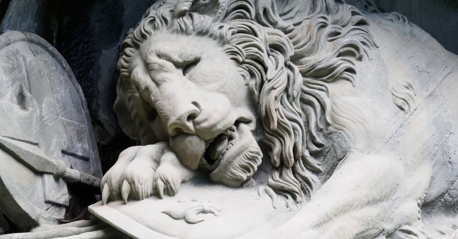 A marble sculpture of a lion with a pain on its face.