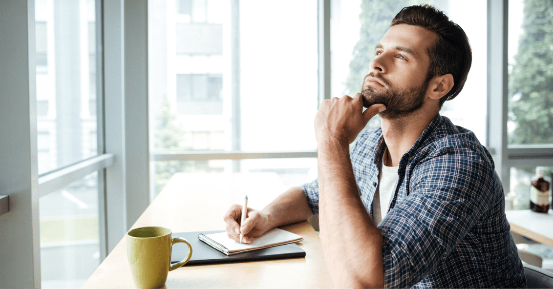 A man sitting in an office thinking and writing ideas down on a pad of paper