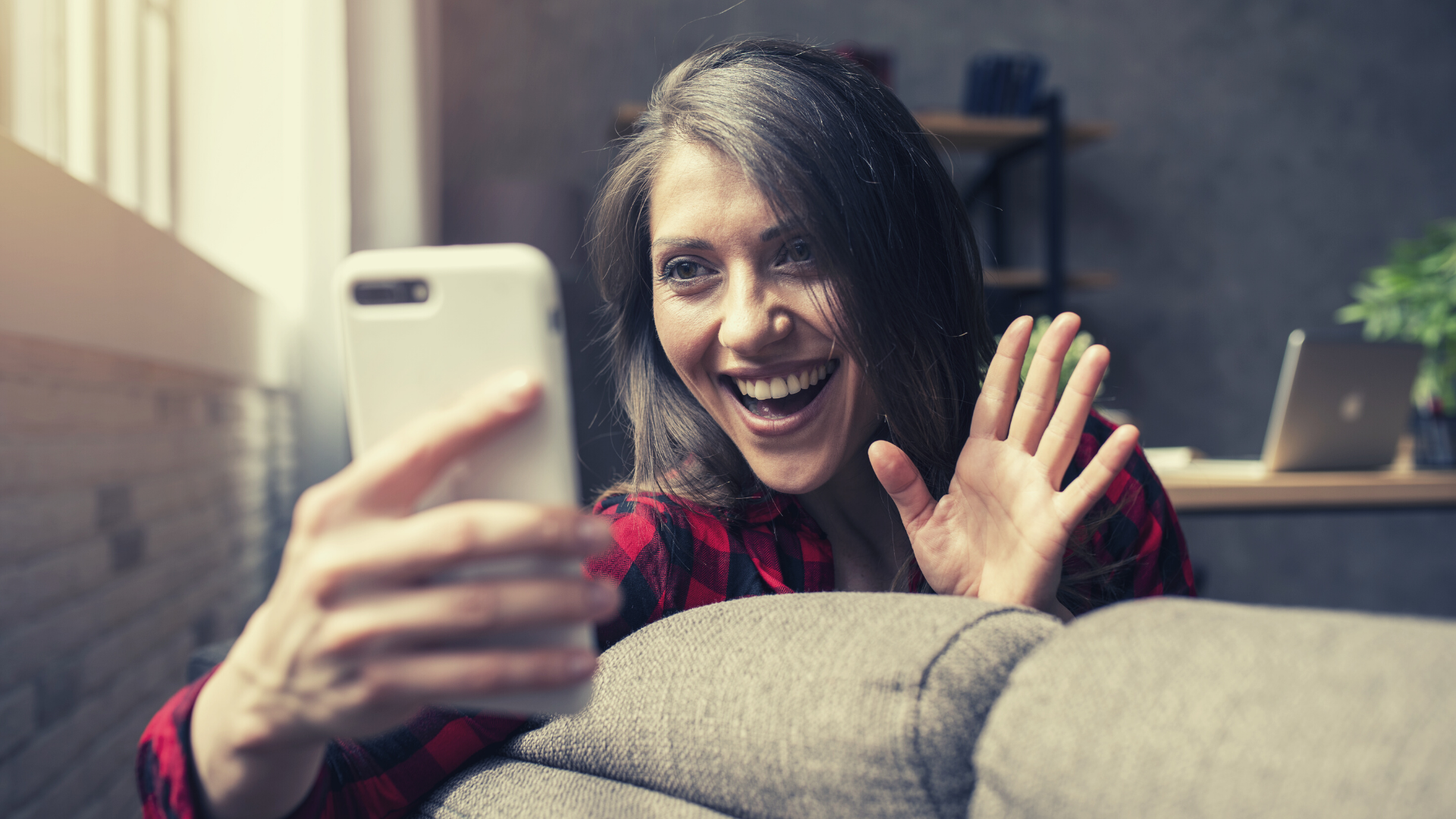 A salesperson smiling and waving while recording a video with their smartphone.