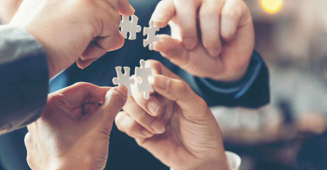 Four hands holding puzzle pieces together as a solutions concept.