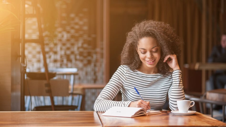 A happy woman writing in a notebook at a kitchen table.