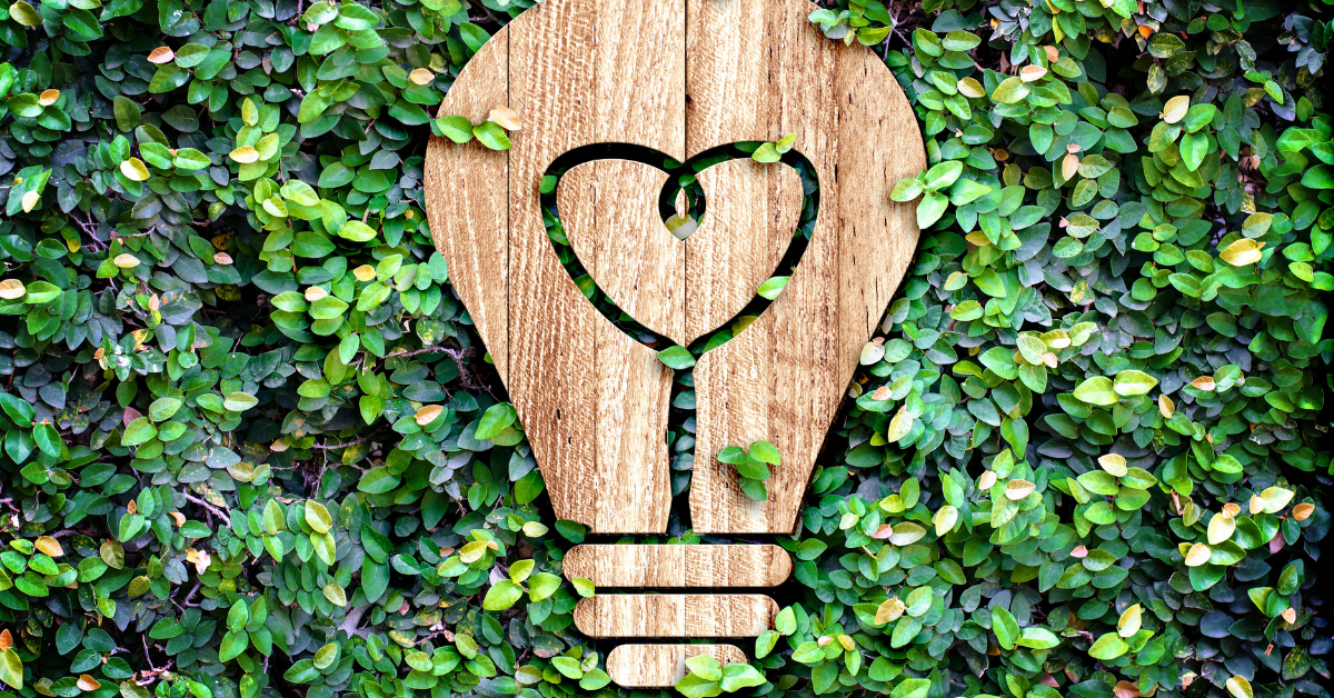 A wooden cutout of a lightbulb against a wall of ivy.